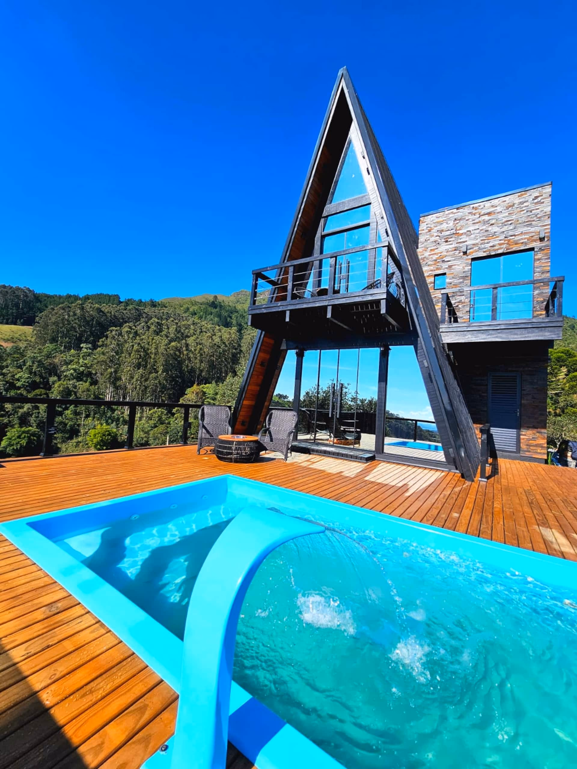 Piscina e deck de madeira do chalé, com vista para o vale, durante o dia
