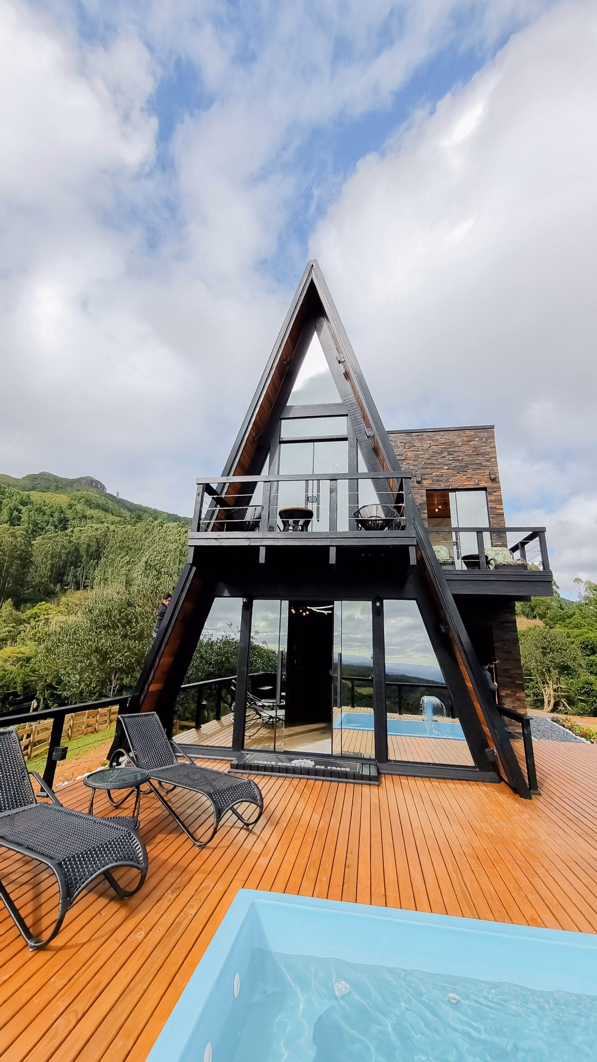 Chalé A-frame ao entardecer, com piscina e deck iluminados