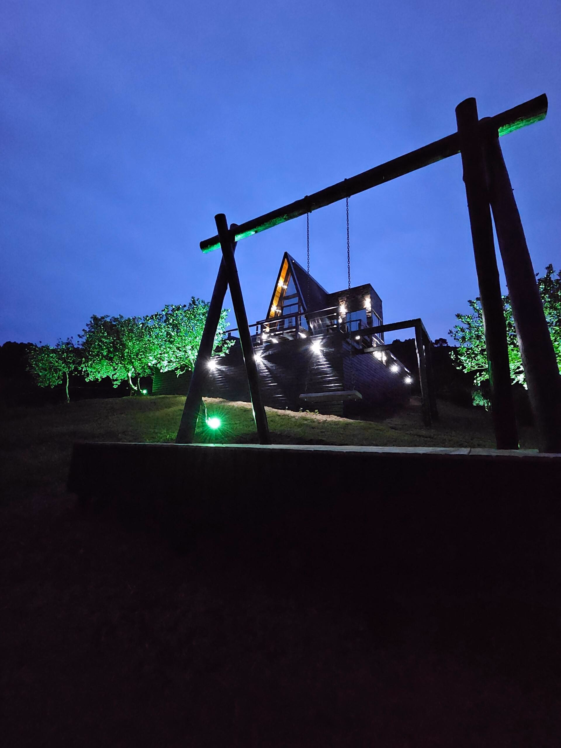 Balanço no jardim ao entardecer, com iluminação verde na vegetação