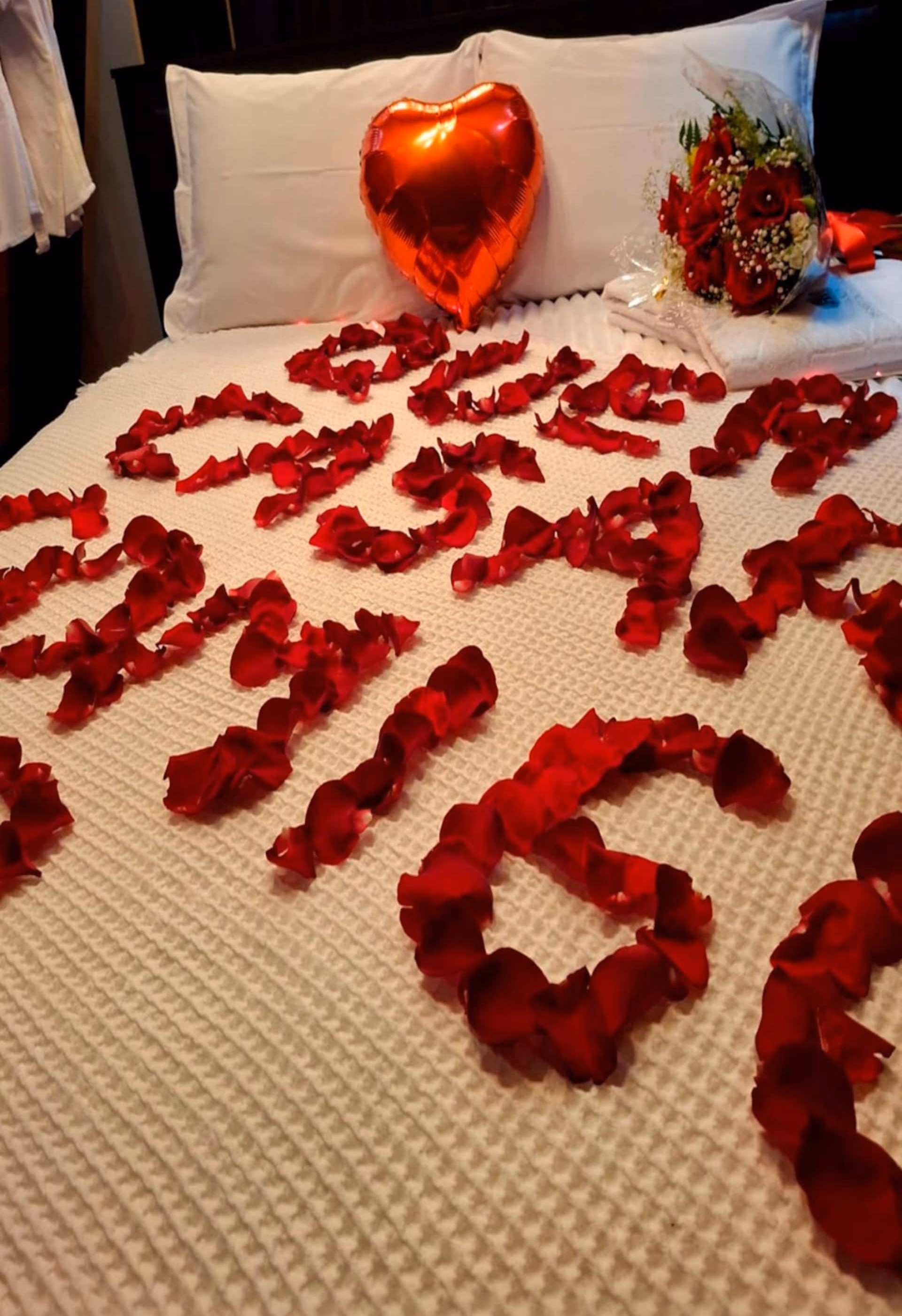 Cama decorada com pétalas de rosa e balão em formato de coração, para datas especiais